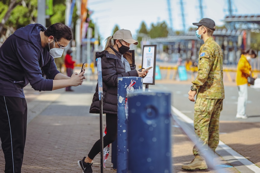 A man and woman scan the QR code while a soldier looks on