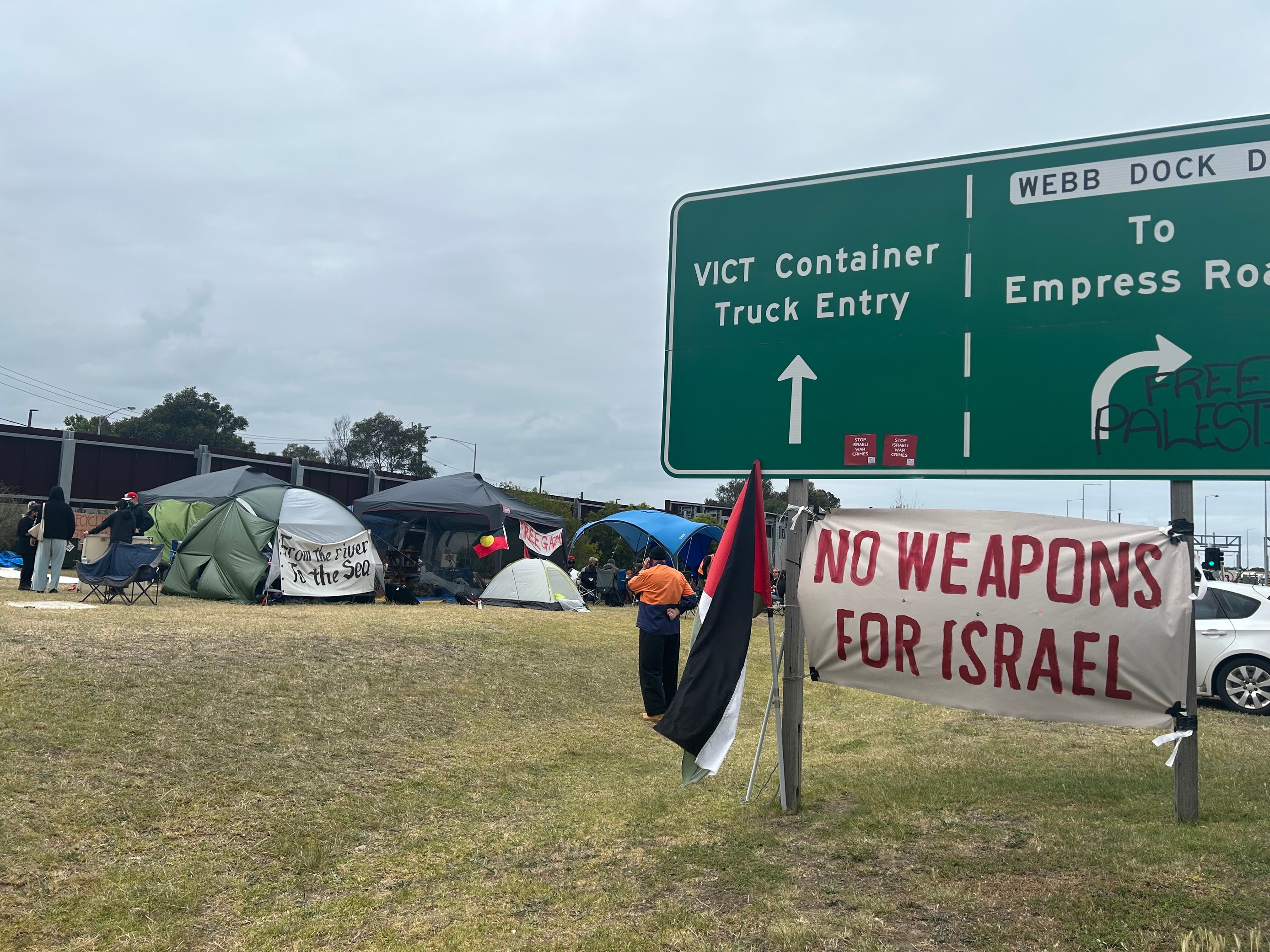 Activists camp site and poster hanging from road sign saying "no weapons for Israel".