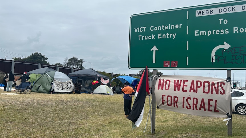 Activists camp site and poster hanging from road sign saying "no weapons for Israel".