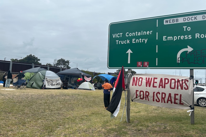 Activists camp site and poster hanging from road sign saying "no weapons for Israel".
