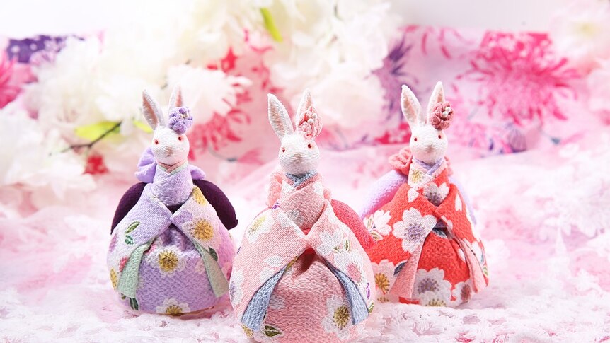 Three small rabbit-like figurines look up  in traditional Japanese dress featuring pink, purple and red flower patterns.