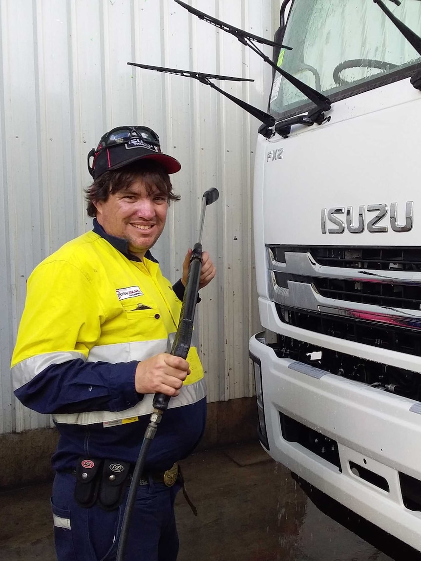 A man in mechanic overalls with a wrench stands by a truck.