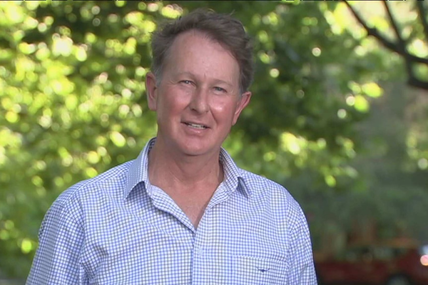 A middle-aged man with short hair stands in a grove.