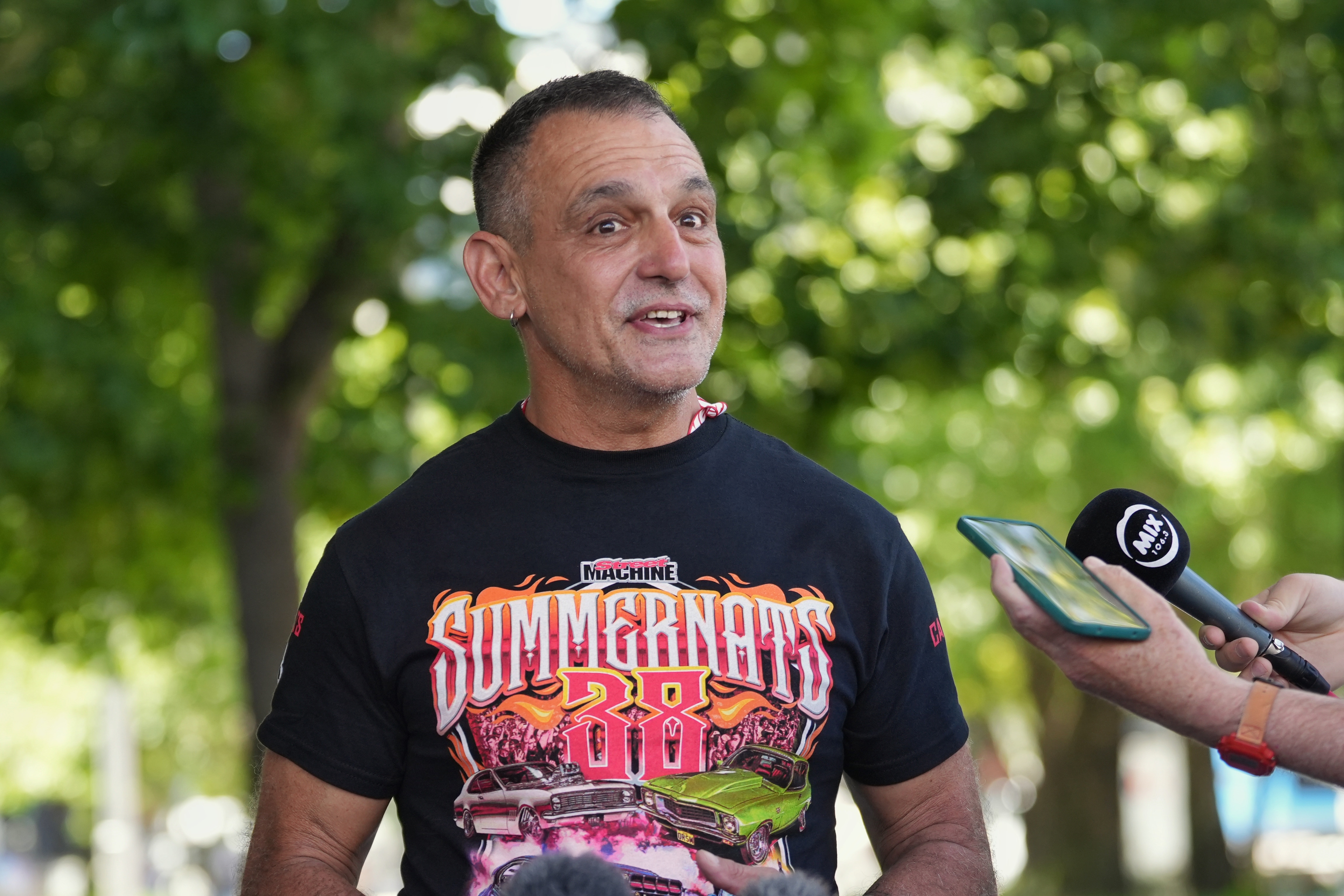 Um homem fala com entusiasmo em uma coletiva de imprensa ao ar livre.