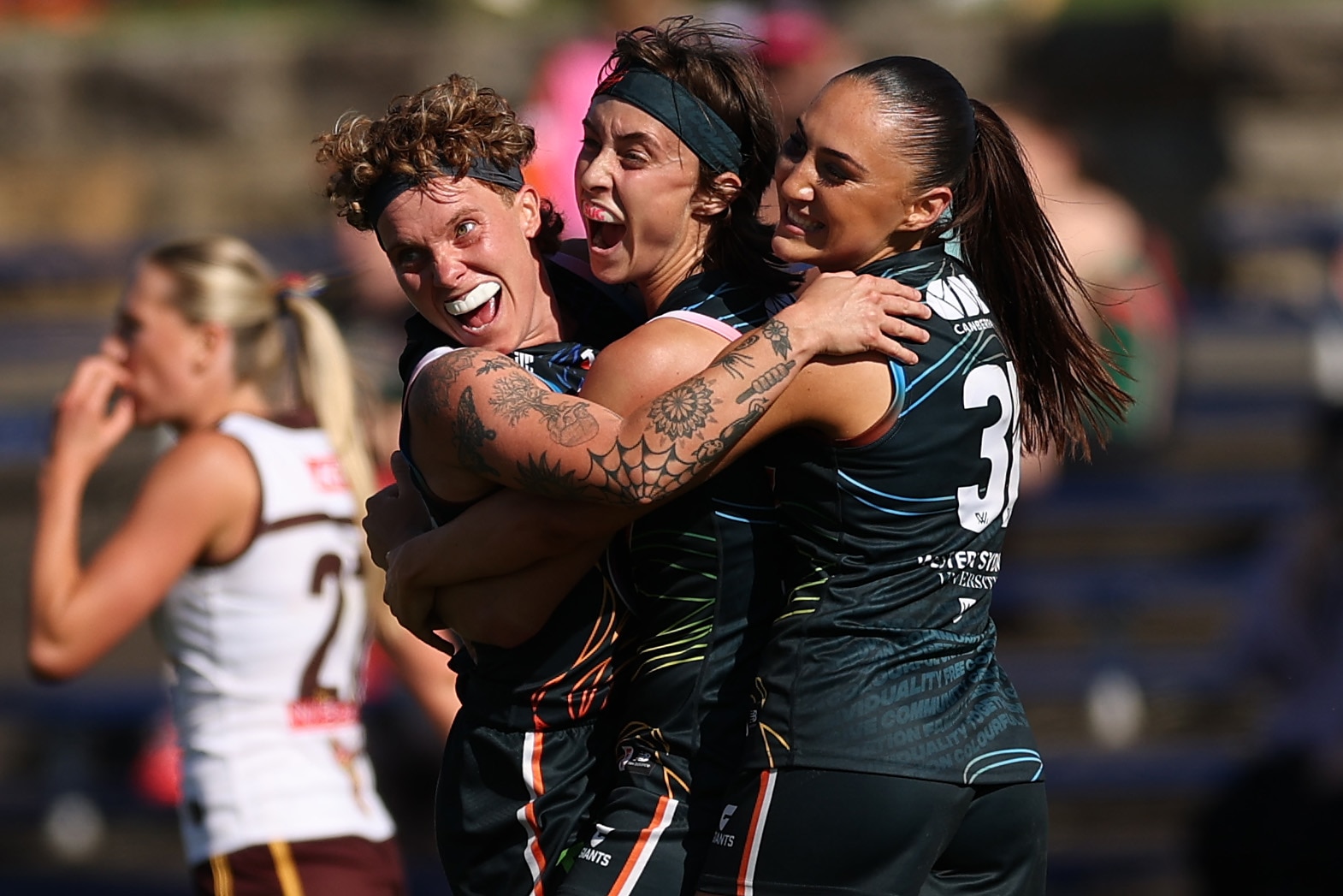 Three Giants AFLW players embrace as they celebrate a win over the Hawks.