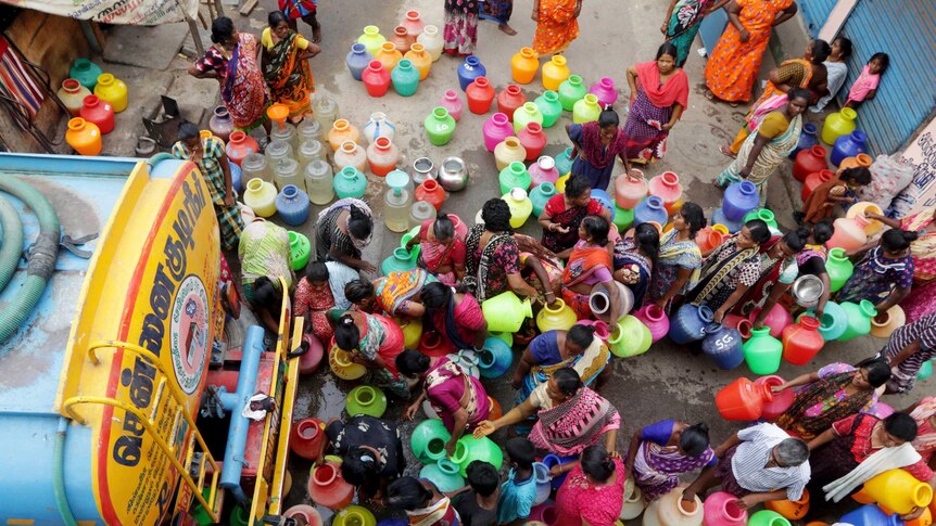 A view from abov of Indian people carrying brightly-coloured vessels for water.