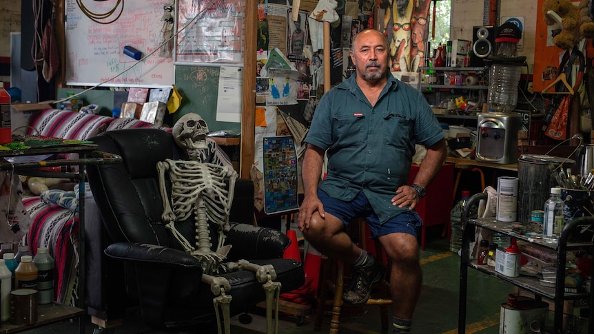 Artist Gordon hookey stands leaned against a stool in his studio