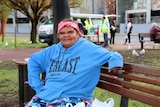 Homeless woman Andrea sitting on a bench with a soup kitchen in the background.