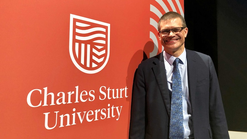 Charles Sturt University Vice Chancellor, Professor Andrew Vann, standing near a poster of the new CSU logo, launched in 2019.