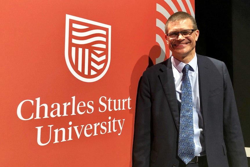 Charles Sturt University Vice Chancellor, Professor Andrew Vann, standing near a poster of the new CSU logo, launched in 2019.