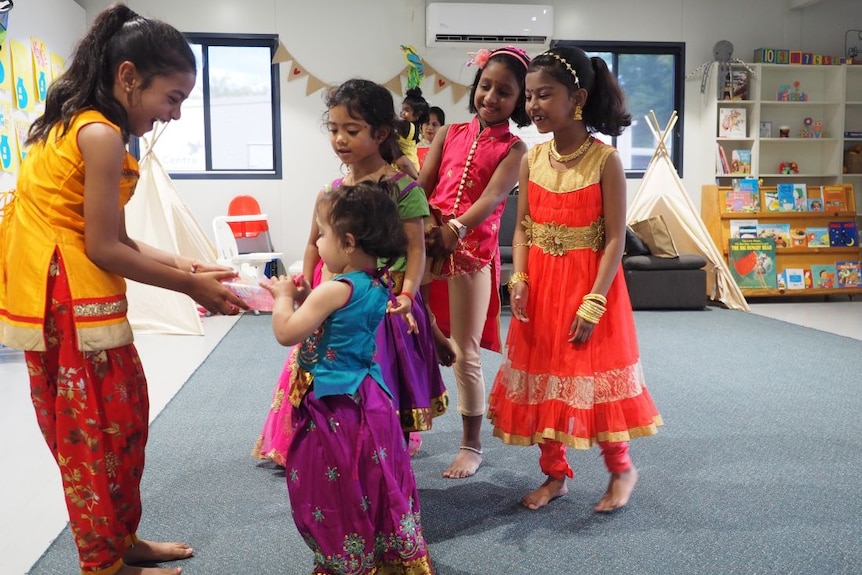 Five young girls in brightly coloured Indian dress play together in a children's classroom.