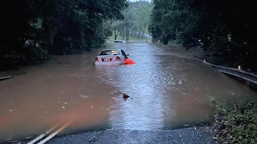 A man checking a car stuck in a flooded causeway