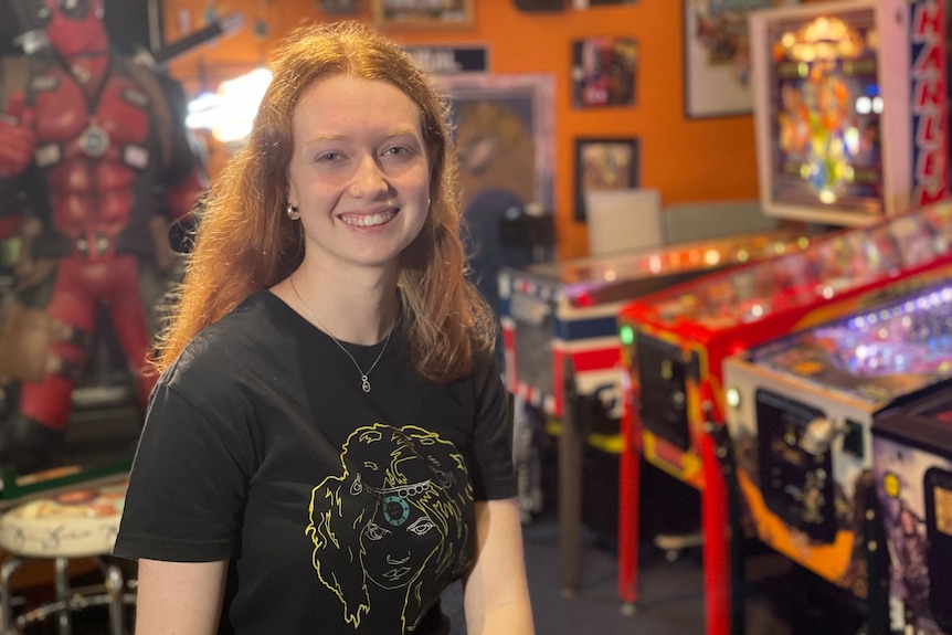 Gold Coast 20-year-old pinball player Emily Cosson sitting in her games room smiling