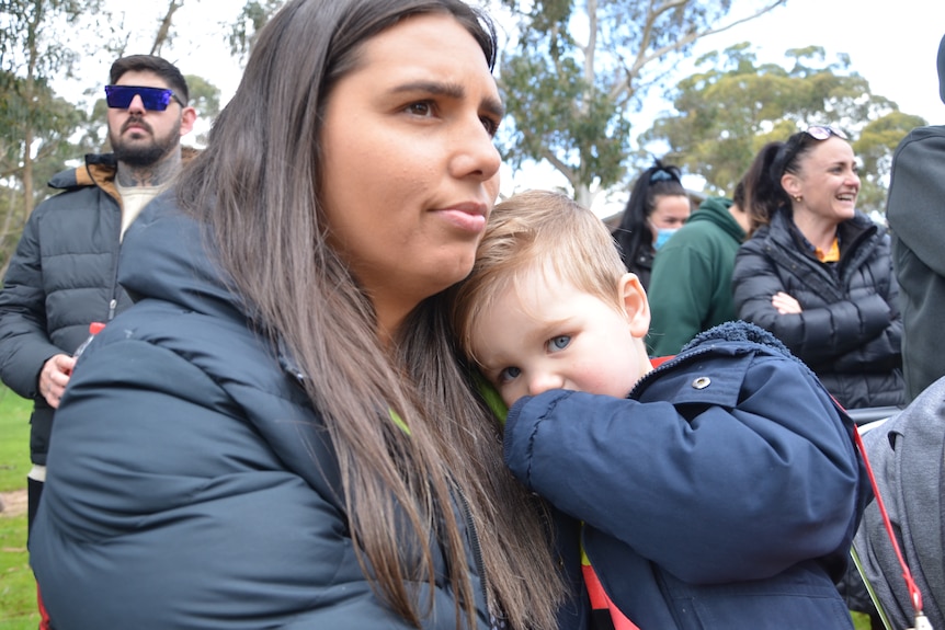A woman with long, dark hair, wearing a parka, cuddles her young son.