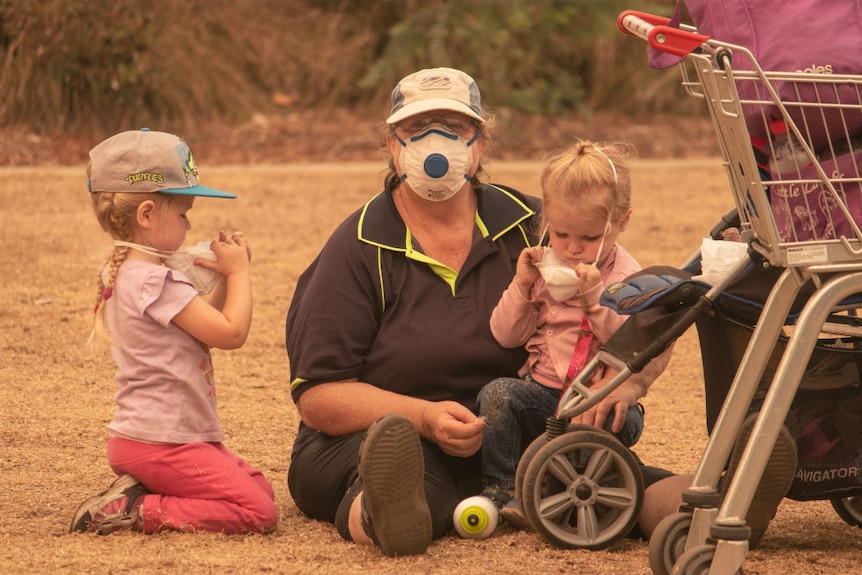 A woman in a mask with two children adjusting masks to their faces.