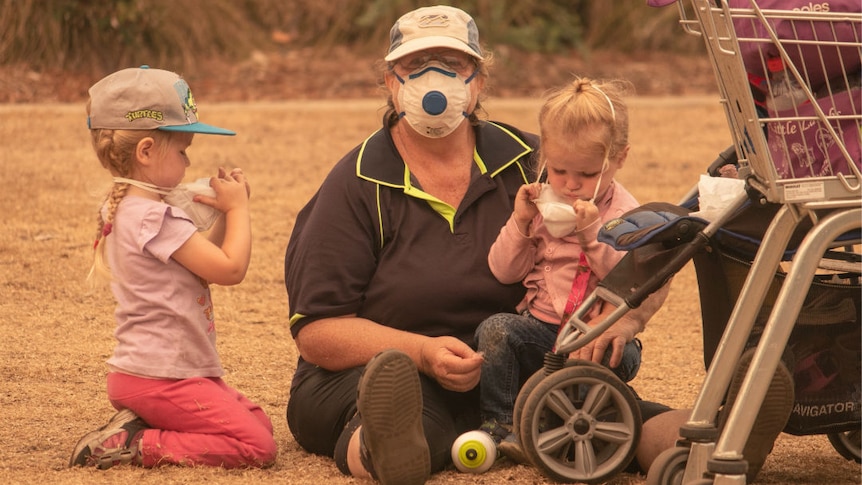 A woman in a mask with two children adjusting masks to their faces.