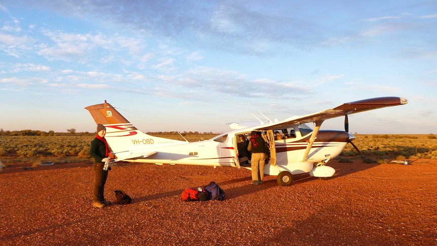 A small aeroplane sitting idle in a red desert.
