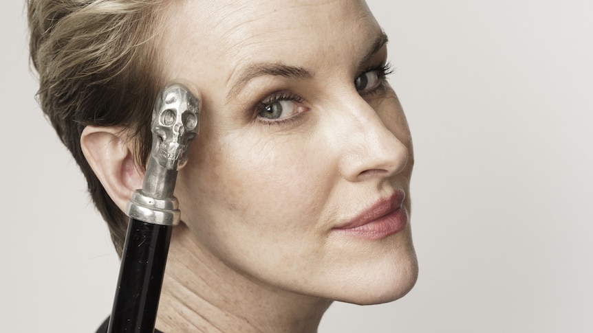 Head shot of woman with cane with skull handle resting on her face.