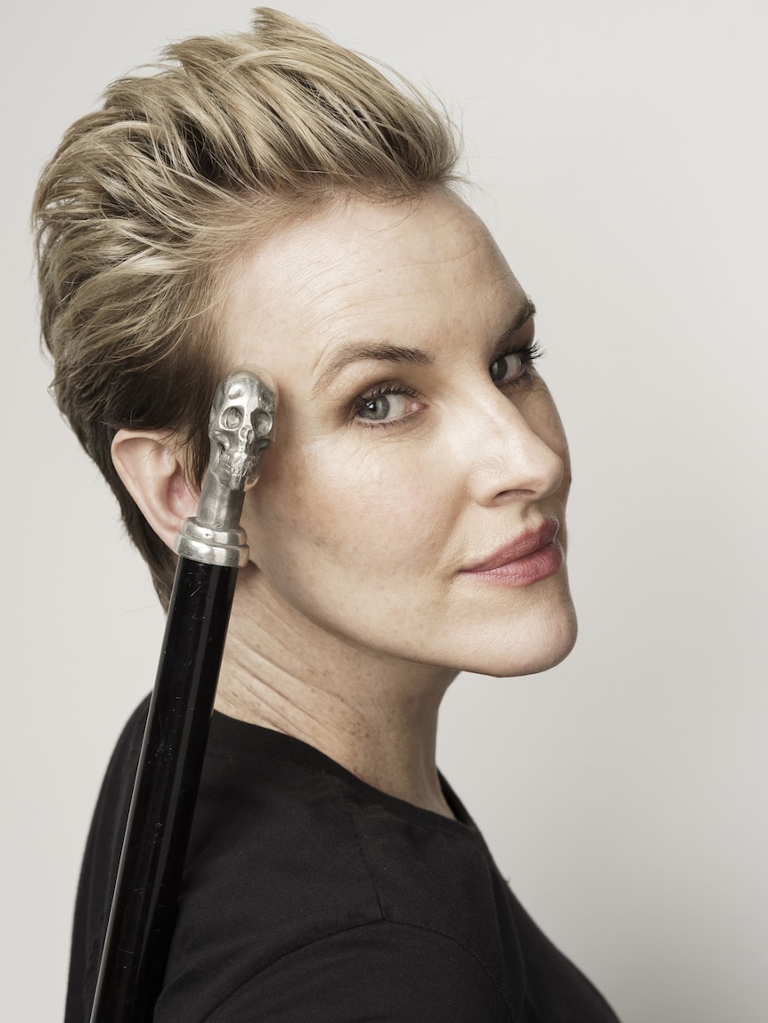 Head shot of woman with cane with skull handle resting on her face.
