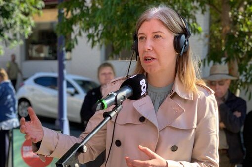 A woman wearing headphones speaks into a microphone as local residents watch on from behind,