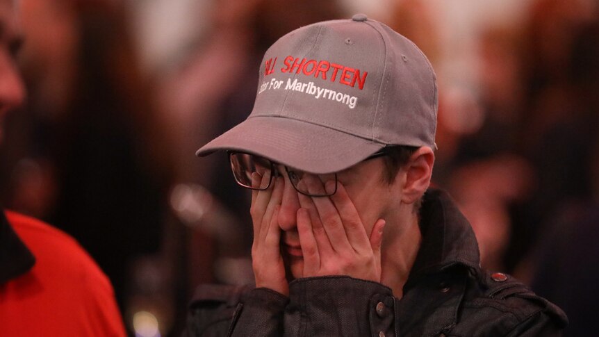 A Labor supporter wearing a Bill Shorten hat rubs his eyes despairingly