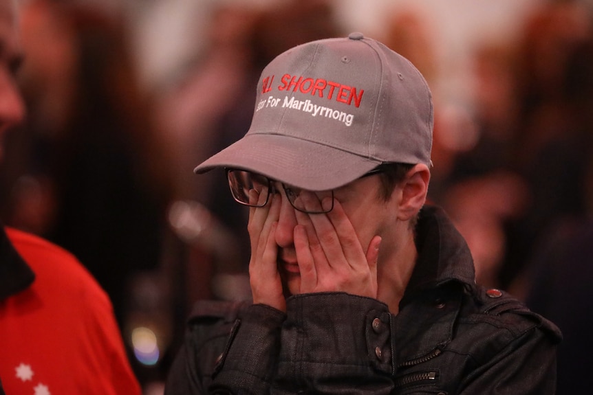 A Labor supporter wearing a Bill Shorten hat rubs his eyes despairingly