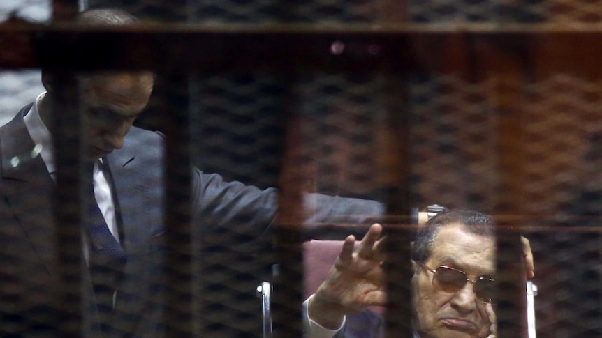 Ousted Egyptian president Hosni Mubarak (right) waves from the defendant's cage
