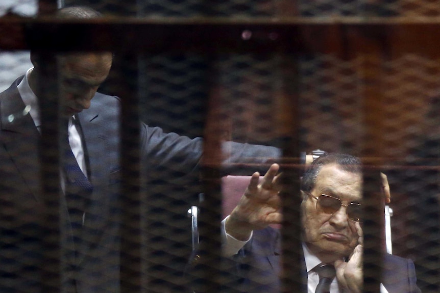 Ousted Egyptian president Hosni Mubarak (right) waves from the defendant's cage