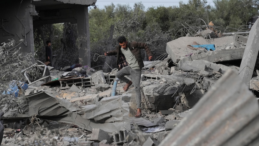 Man walks barefoot on rubble and debris of his home. 