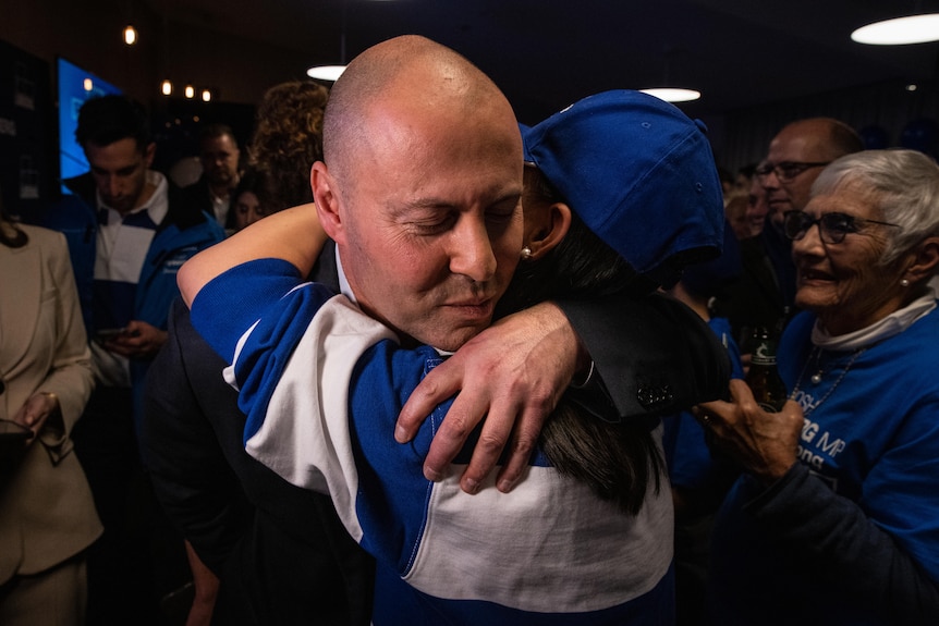 A man in a cap give Frydenberg a hug