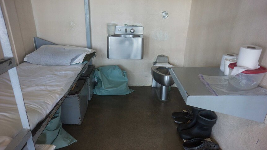 The interior of a prison cell, showing bunk beds, a desk, toilet and wash basin.