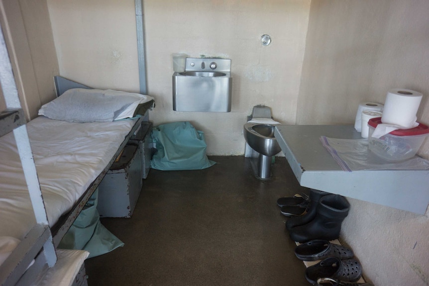 The interior of a prison cell, showing bunk beds, a desk, toilet and wash basin.