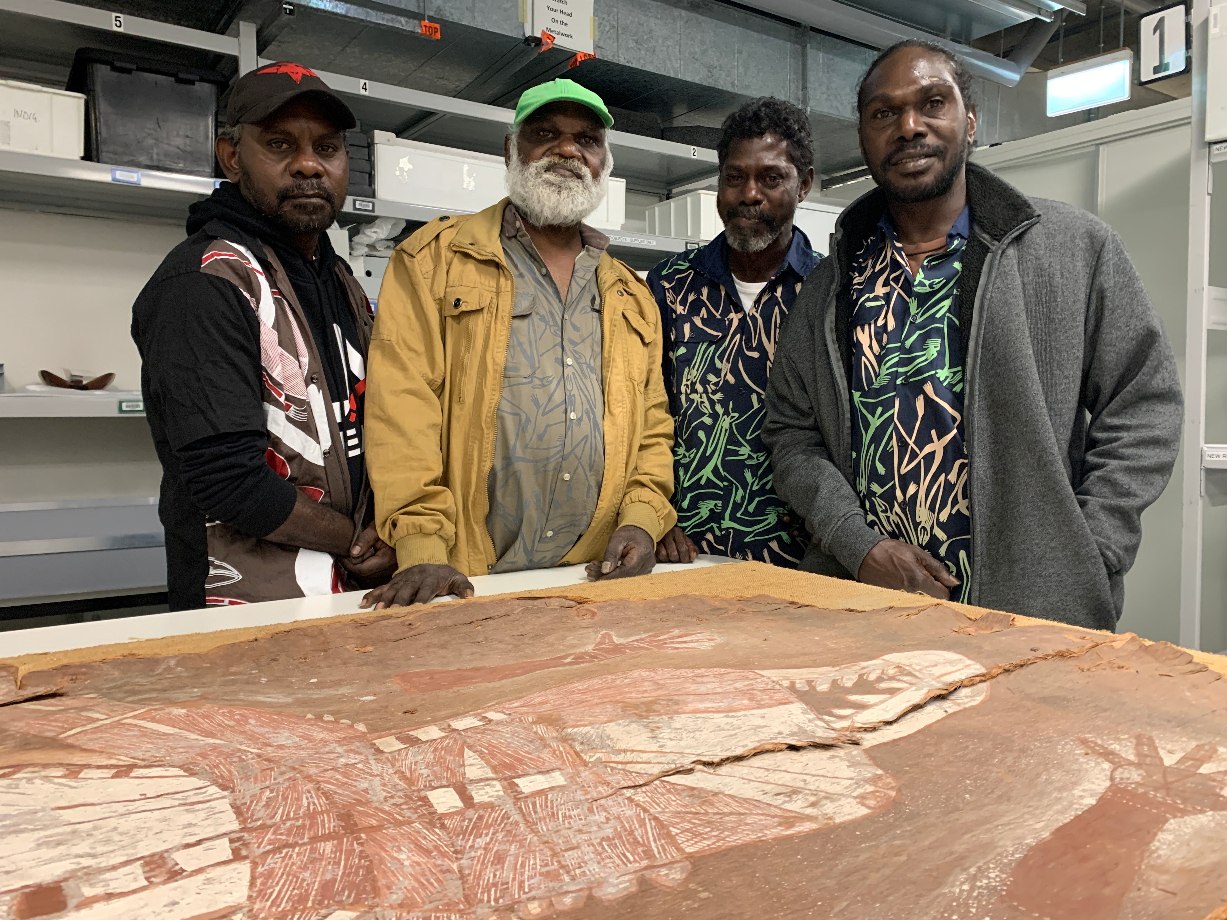 Four Arnhem Land men stand with a prized bark painting.