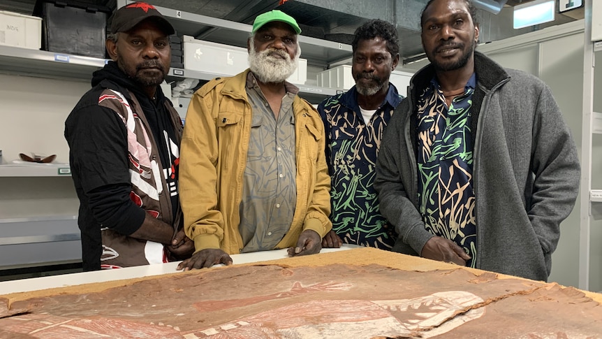 Four Arnhem Land men stand with a prized bark painting.