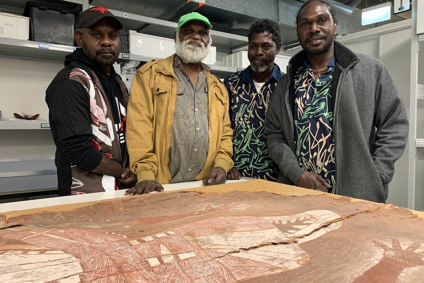 Four Arnhem Land men stand with a prized bark painting.