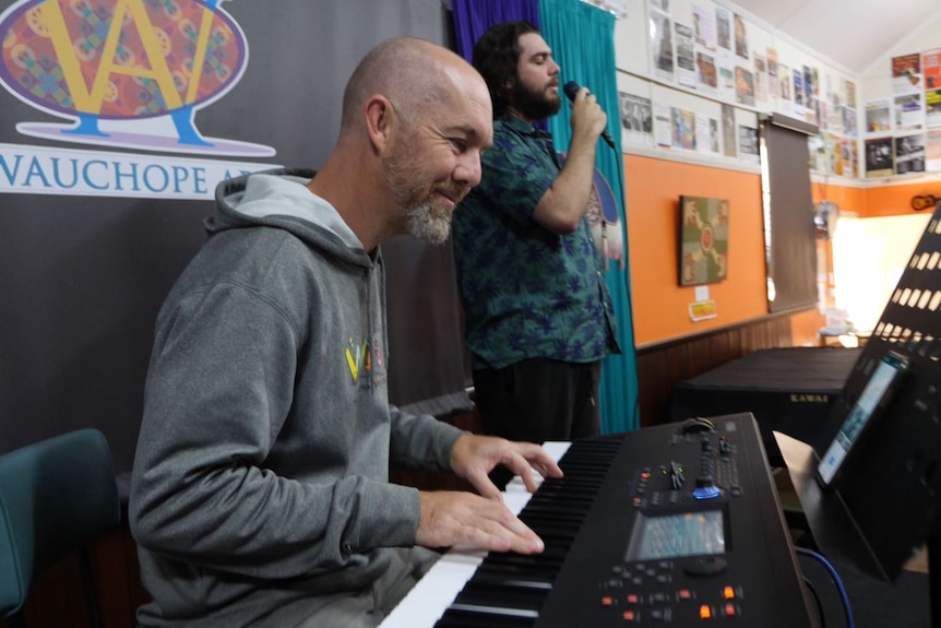 A man playing keyboard with a young man singing into a microphone