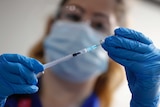 A woman holds up a needle next to a vial during a trial of the Pfizer COVID-19 vaccine.