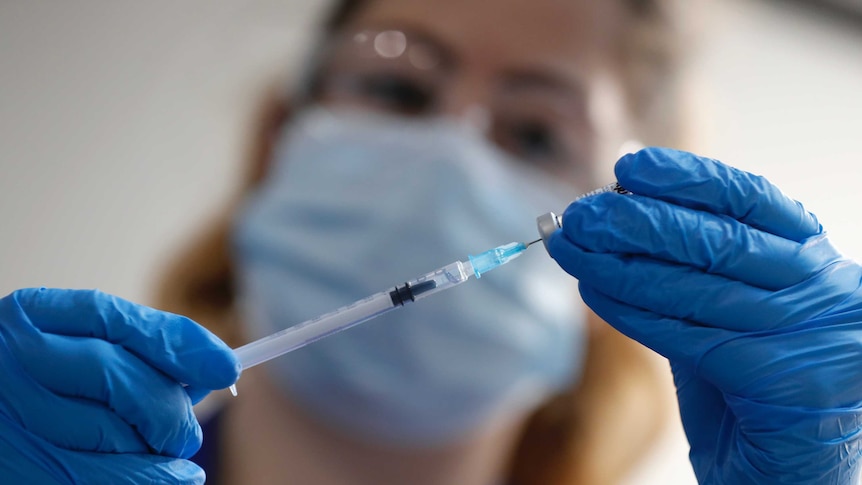 A woman holds up a needle next to a vial.