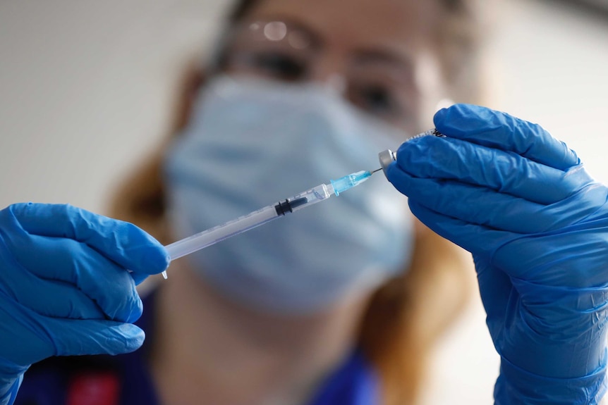 A woman holds up a needle next to a vial.