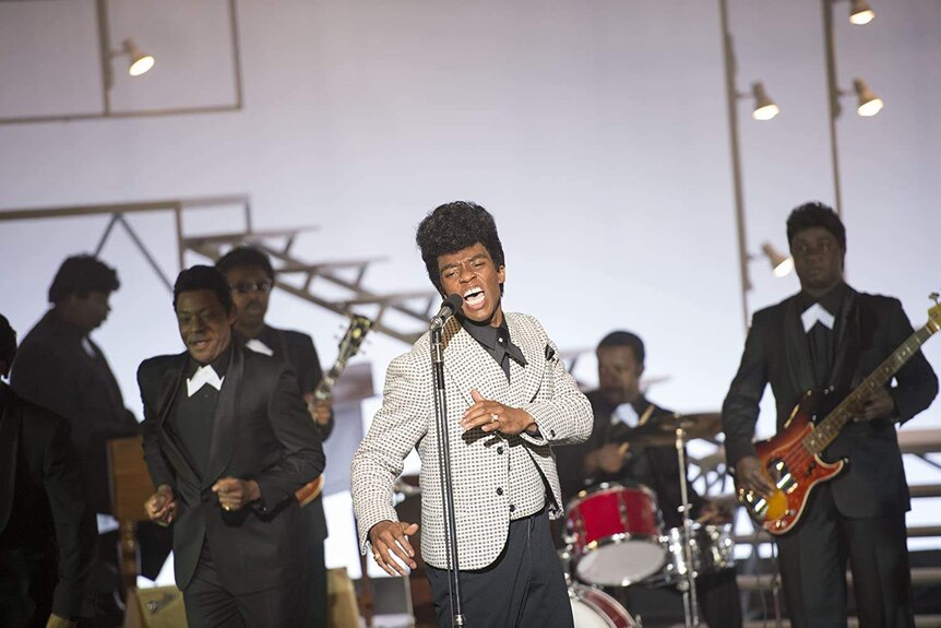 Still from the film Get on Up with Chadwick Boseman playing the soul singer James Brown performing on stage with a band