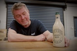 A man looks at a bottle on a table