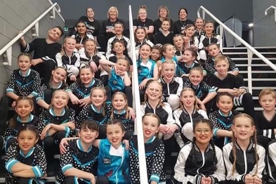 Forty students in black, white and blue costumes sit on stairs.