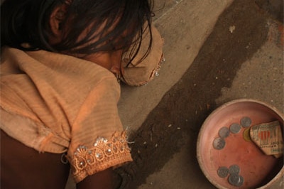 A girl sleeps beside a begging bowl on the ground at a rice market on in Dhaka, Bangladesh, 2008.