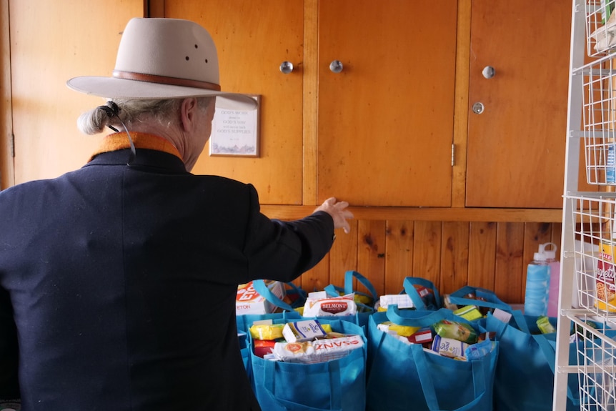 A man sorts through bags of groceries with shelves of tins on the side wall.