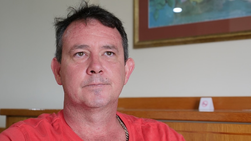 Close up of middle-aged man looking concerned, wearing red t-shirt.