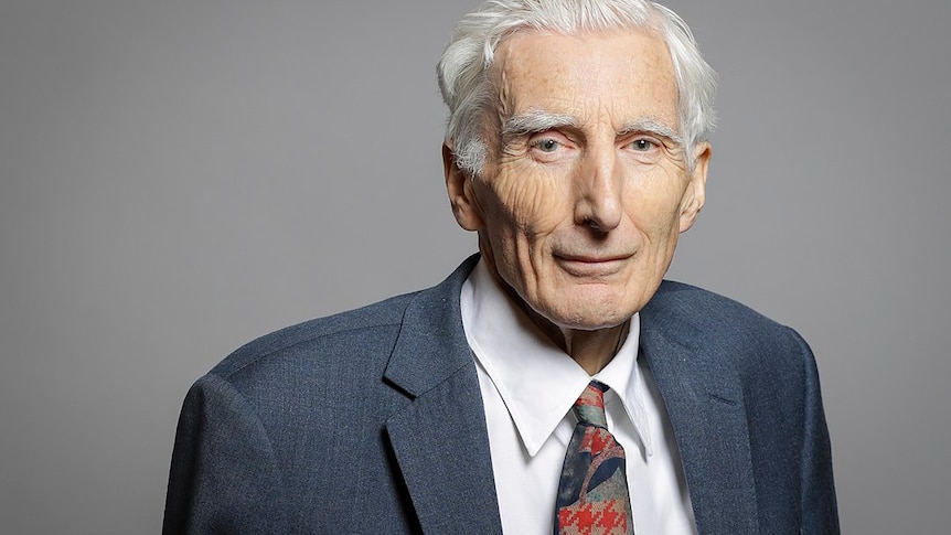 An elderly man in a smart blue suit looks at the camera with a kind expression