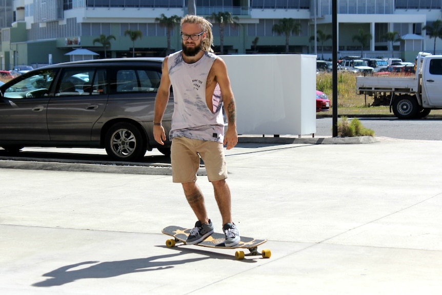 Man moving on a longboard skateboard, looking at the camera.