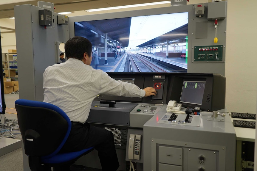 Minoru Mukaiya sits in front of a screen showing a train simulation