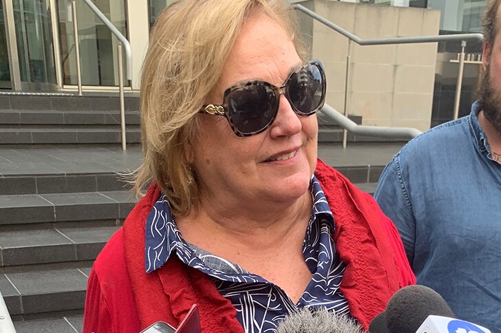 A headshot of a woman standing outside court wearing sunglasses and talking to the media.