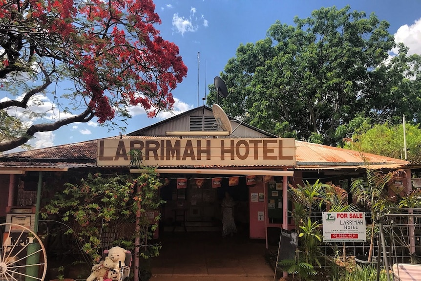 A country pub with a large sign sits underneath trees.